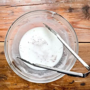 Chicken being dipped in buttermilk and seasoned flour for extra crispy hot honey chicken sandwich.