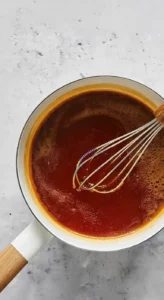 Hot honey sauce simmering in a saucepan with a whisk.